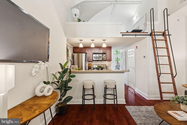 kitchen with appliances with stainless steel finishes, dark wood-type flooring, a peninsula, tasteful backsplash, and a kitchen breakfast bar