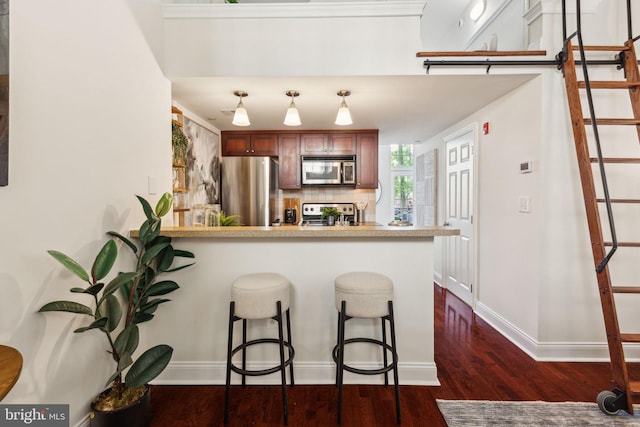 kitchen with stainless steel appliances, a peninsula, dark wood-style floors, a kitchen bar, and backsplash