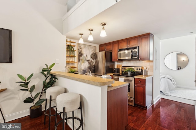 kitchen featuring appliances with stainless steel finishes, dark wood-type flooring, baseboards, a kitchen bar, and tasteful backsplash