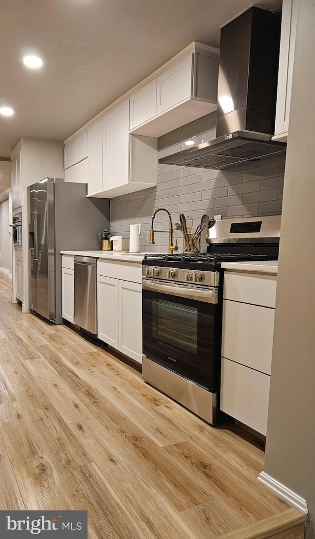 2563 Emerald St, Philadelphia, PA 19125 - kitchen with appliances with stainless steel finishes, wall chimney exhaust hood, light wood-style floors, white cabinetry, and tasteful backsplash