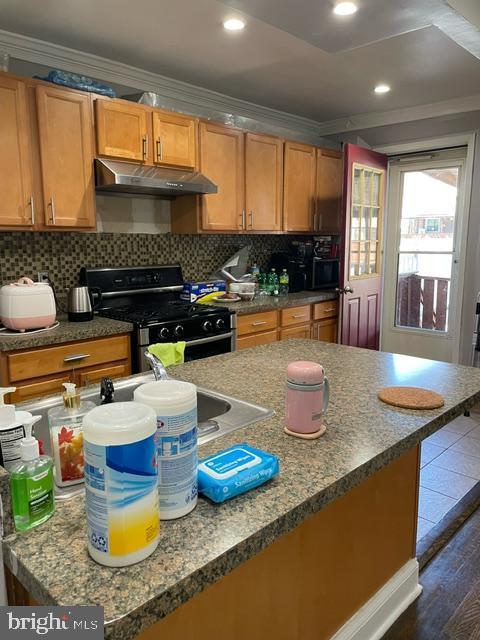 3339 Ashville St, Philadelphia, PA 19136 - kitchen with under cabinet range hood, stainless steel gas stove, crown molding, dark wood finished floors, and tasteful backsplash