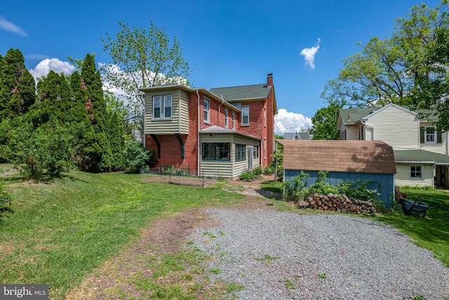 back of property featuring a chimney, brick siding, an outbuilding, and a yard