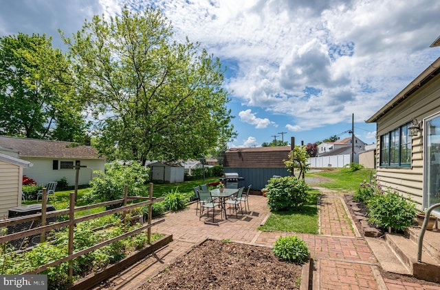 view of yard with a storage unit, a patio, an outbuilding, a garden, and fence