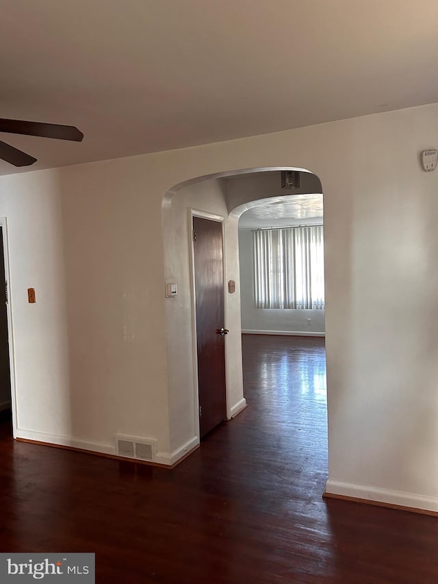 corridor with arched walkways, dark wood-style floors, and baseboards