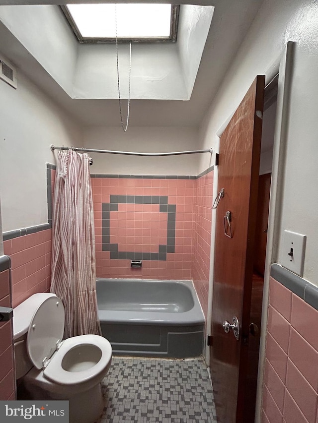 bathroom with tile walls, toilet, shower / bath combination with curtain, tile patterned floors, and a wainscoted wall