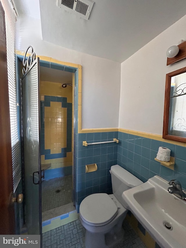 bathroom featuring a shower stall, a sink, toilet, a wainscoted wall, and tile walls
