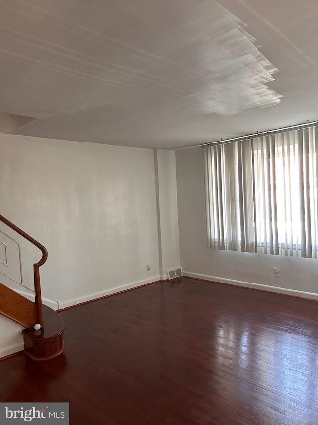 empty room with baseboards, wood finished floors, and stairs