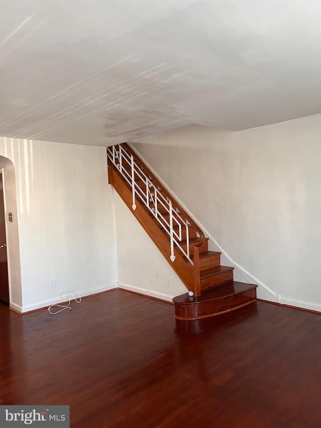 below grade area featuring baseboards, stairs, wood finished floors, and arched walkways