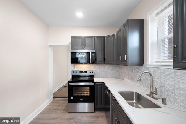 kitchen featuring appliances with stainless steel finishes, a sink, backsplash, and light stone countertops