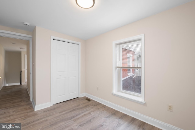 unfurnished bedroom featuring light wood-type flooring, baseboards, and a closet