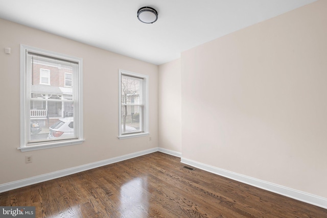 spare room with baseboards and dark wood-type flooring
