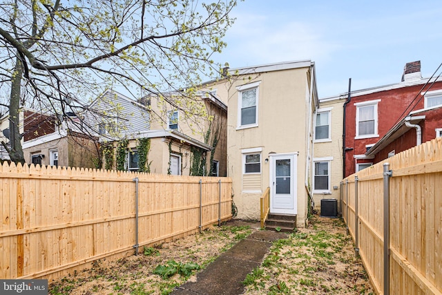 rear view of property with entry steps, central AC, a fenced backyard, and stucco siding