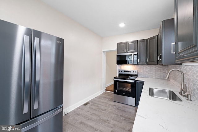 kitchen with appliances with stainless steel finishes, a sink, light stone counters, backsplash, and baseboards