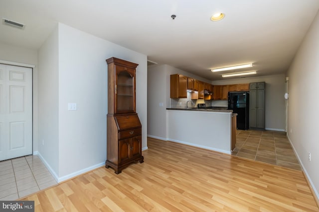 kitchen featuring freestanding refrigerator, dark countertops, a sink, a peninsula, and light wood finished floors