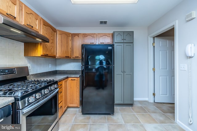 kitchen featuring freestanding refrigerator, stainless steel gas range, under cabinet range hood, decorative backsplash, and light tile patterned floors
