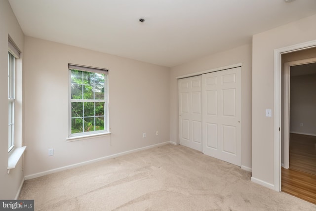 unfurnished bedroom with baseboards, light carpet, and a closet