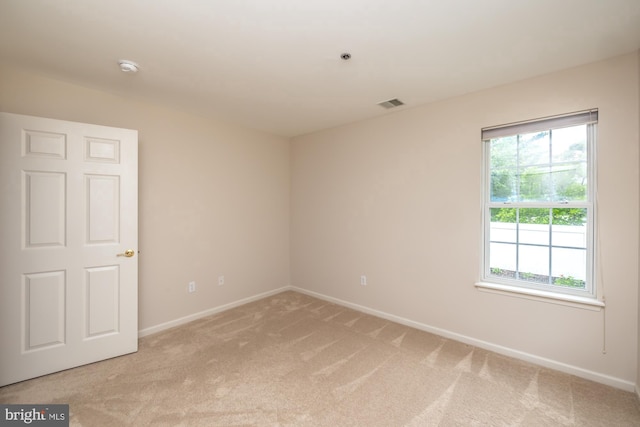 spare room featuring light carpet, baseboards, and a smoke detector