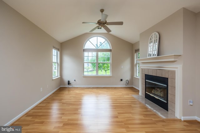 unfurnished living room with light wood finished floors, a ceiling fan, a tiled fireplace, lofted ceiling, and baseboards