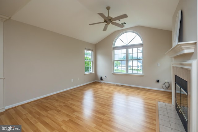 unfurnished living room with a tiled fireplace, light wood finished floors, a ceiling fan, lofted ceiling, and baseboards