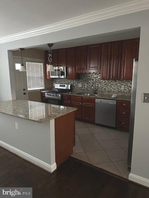 kitchen with stainless steel appliances, a sink, crown molding, tasteful backsplash, and light wood-style flooring
