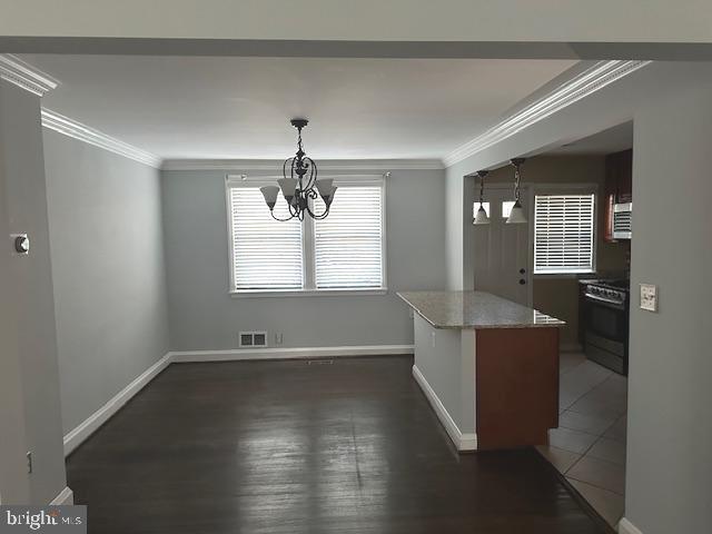 unfurnished dining area with a chandelier, ornamental molding, baseboards, and dark wood finished floors