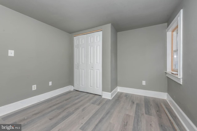 unfurnished bedroom featuring wood finished floors, baseboards, and a closet
