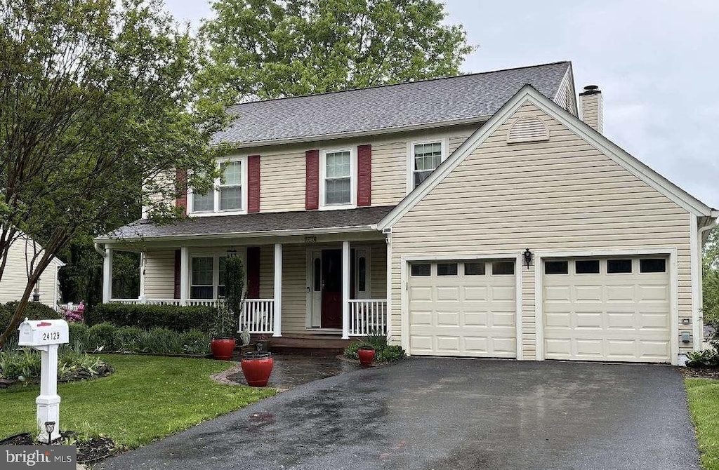 traditional home with driveway, a chimney, covered porch, an attached garage, and a front yard
