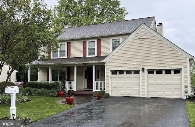 traditional home with driveway, a chimney, covered porch, an attached garage, and a front yard