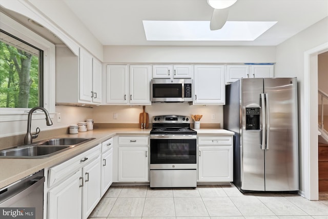kitchen with appliances with stainless steel finishes, a sink, a skylight, and white cabinetry