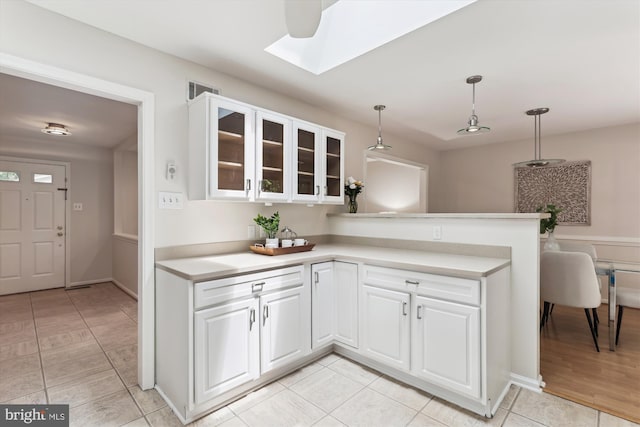kitchen with a skylight, glass insert cabinets, light countertops, light tile patterned flooring, and pendant lighting