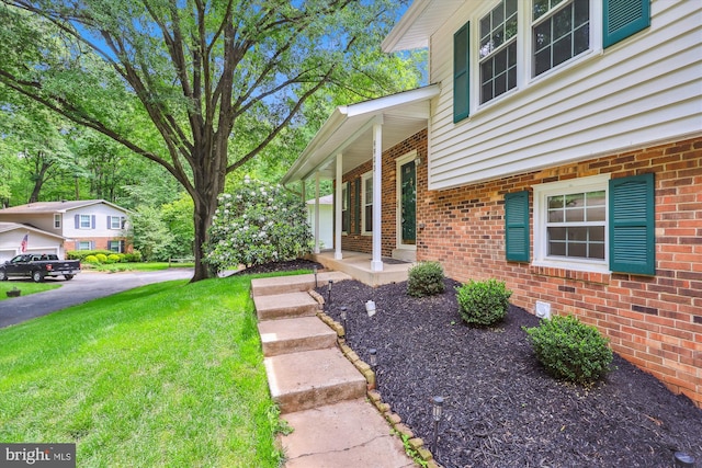 property entrance with brick siding, a lawn, and covered porch