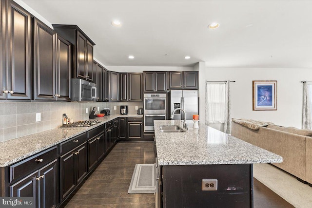 2121 River Heritage Blvd, Dumfries, VA 22026 - kitchen with stainless steel appliances, open floor plan, a sink, a kitchen island with sink, and light stone counters