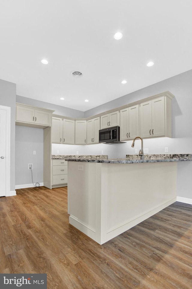 kitchen featuring wood finished floors, light stone counters, baseboards, a sink, and recessed lighting
