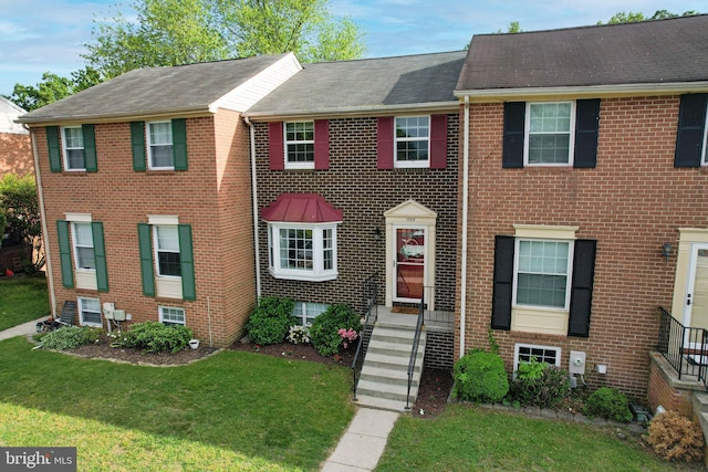 multi unit property featuring brick siding, a front lawn, and roof with shingles