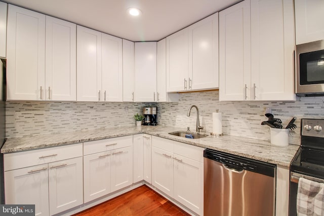 kitchen with appliances with stainless steel finishes, a sink, white cabinetry, light wood finished floors, and light stone countertops