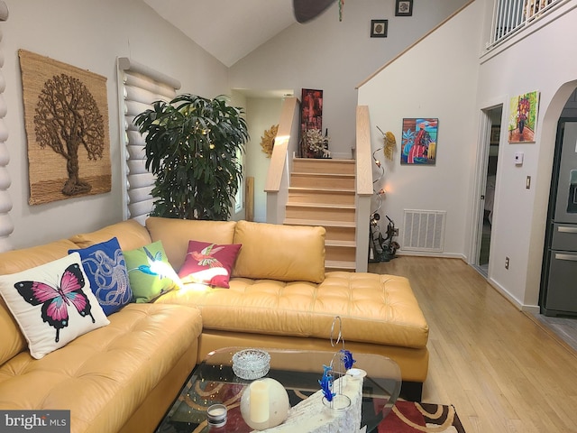 living room with wood finished floors, stairs, arched walkways, high vaulted ceiling, and baseboards