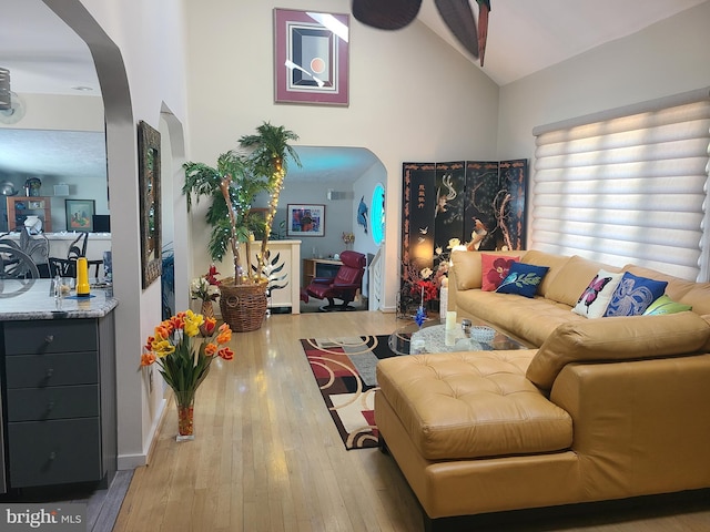 living area with arched walkways, vaulted ceiling, and hardwood / wood-style floors
