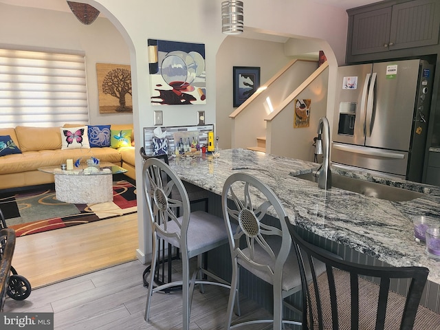 kitchen featuring stainless steel fridge, light stone counters, arched walkways, and a breakfast bar