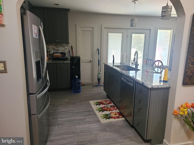 kitchen featuring stainless steel appliances, arched walkways, a sink, dark wood-style floors, and tasteful backsplash