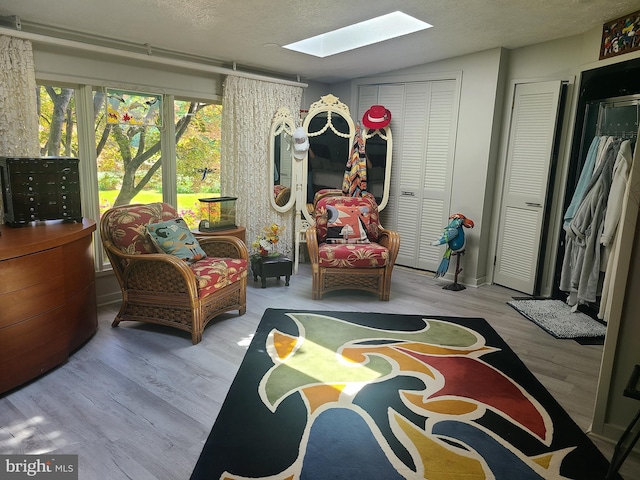 living area featuring a skylight, wood finished floors, a textured ceiling, and lofted ceiling