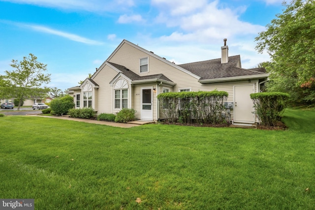 back of property with a chimney, a lawn, and roof with shingles