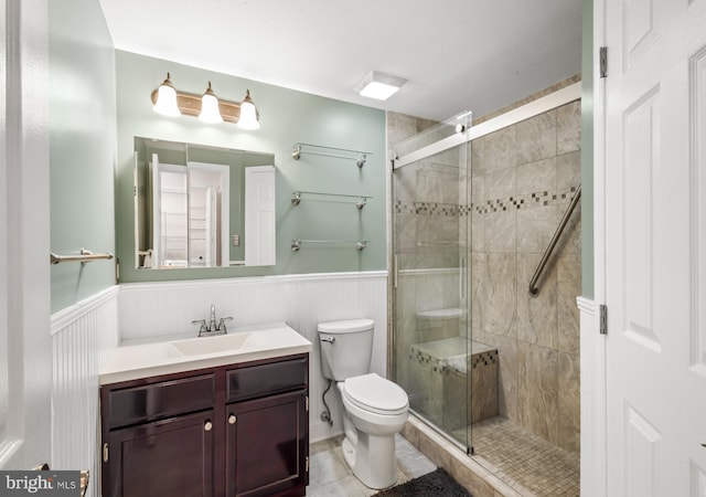 full bathroom with a stall shower, a wainscoted wall, toilet, vanity, and tile patterned flooring