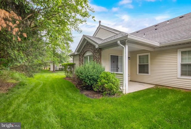 rear view of property with a shingled roof, a lawn, and a patio area