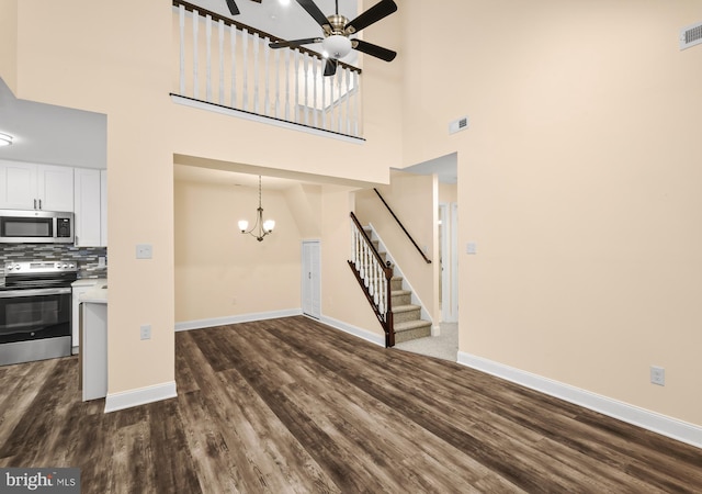 unfurnished living room featuring stairs, ceiling fan, dark wood-style floors, a high ceiling, and baseboards