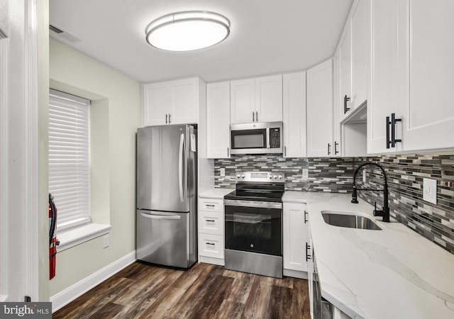 kitchen featuring appliances with stainless steel finishes, a sink, tasteful backsplash, dark wood-style flooring, and white cabinetry