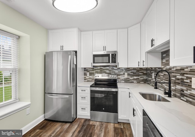 kitchen featuring appliances with stainless steel finishes, a sink, tasteful backsplash, dark wood-type flooring, and white cabinetry