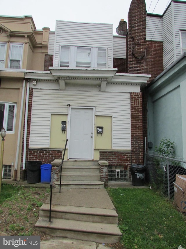 back of property with brick siding, fence, and entry steps