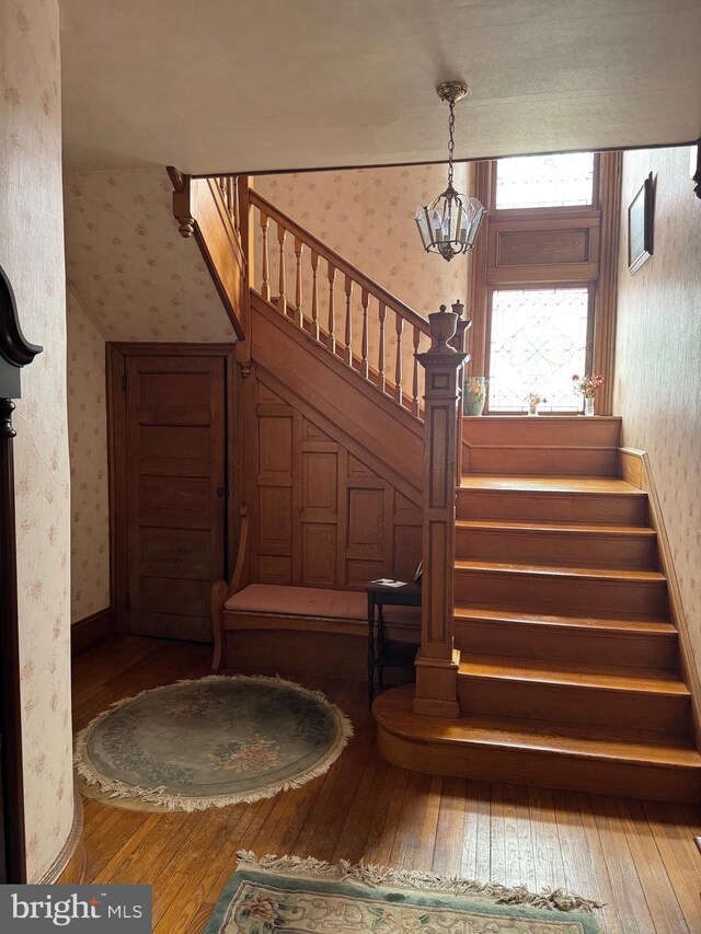 stairway featuring wallpapered walls, hardwood / wood-style flooring, and a chandelier