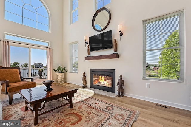 living area with plenty of natural light, a glass covered fireplace, wood finished floors, baseboards, and a high ceiling