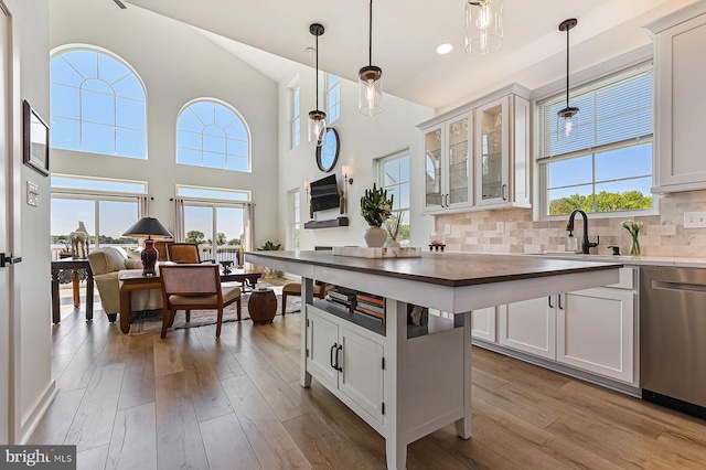 kitchen featuring a sink, stainless steel dishwasher, hardwood / wood-style flooring, glass insert cabinets, and high vaulted ceiling